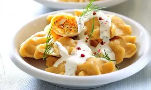 Elegancki obiad dla gości: pyszne pierogi z farszem, polane sosem śmietanowym, ozdobione koperkiem i pieprzem.