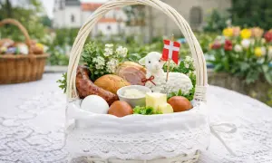W koszyczku wielkanocnym: biała kiełbasa, jajka, masło, chleb, baranek z flagą Danii i bukszpan.