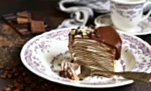 Kawałek czekoladowego tortu naleśnikowego z kremem mascarpone, polany czekoladą i posypany migdałami.