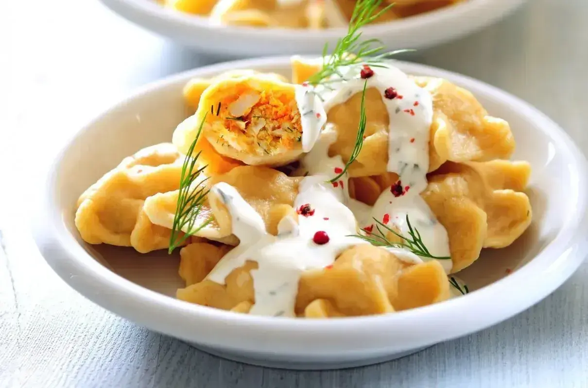 Elegancki obiad dla gości: pyszne pierogi z farszem, polane sosem śmietanowym, ozdobione koperkiem i pieprzem.