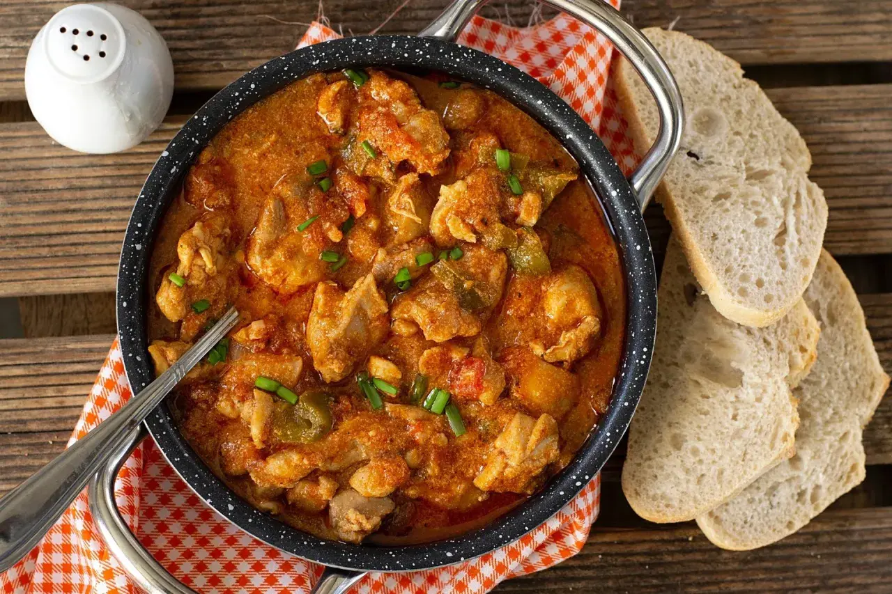 Pyszny gulasz z indyka w sosie pomidorowym, posypany szczypiorkiem, podany z chlebem.